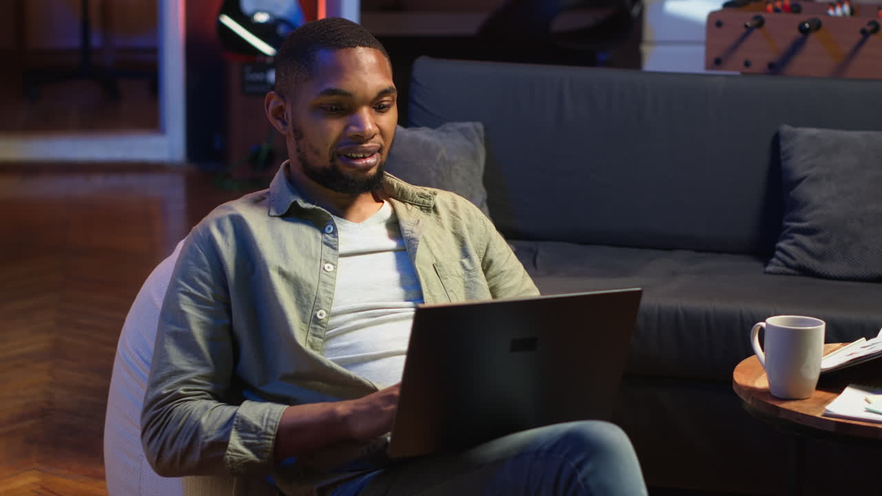 Vertical Video Adult guy typing on laptop laying on couch at his stylish loft space