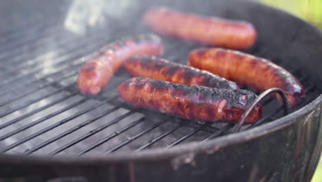 slow motion of tongs picking up a gristly sausage from smokey bbq grill