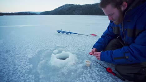 el hombre noruego se dedica a la pesca de invierno poniendo el cebo en el anzuelo de una caña de pescar en noruega