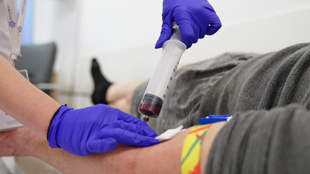 Filling the large syringe with patient's blood. Close up. Medic in blue latex gloves takes blood from vein.