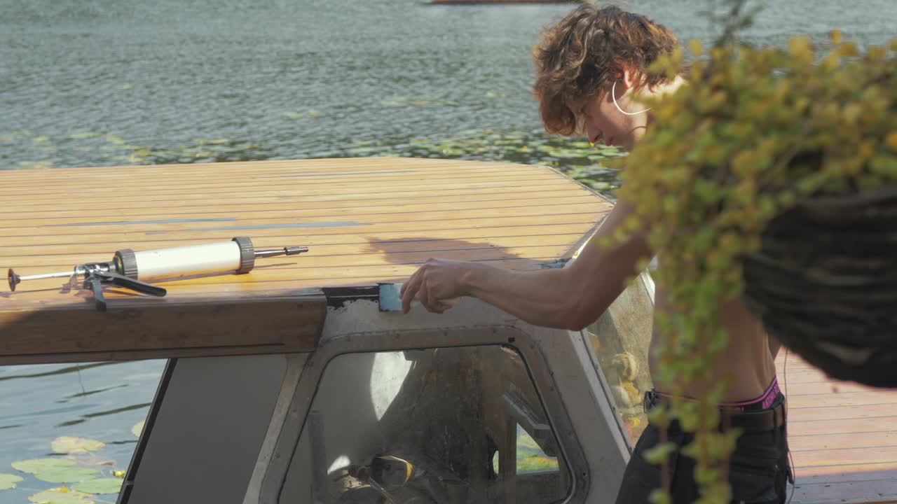 Giovane al lavoro che sigilla il tetto di una cabina di barca in legno per prevenire perdite, usando silicone impermeabile Sika Flex.