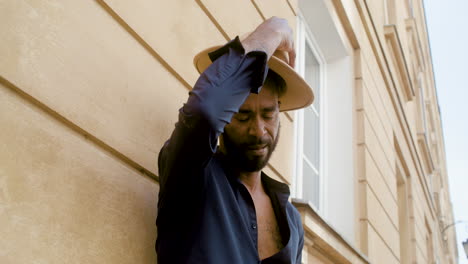 afro caribbean man putting his panama hat on while leaning on the wall with one leg up in the old town street 1