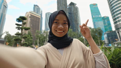 happy young muslim woman in hijab taking a selfie in an urban cityscape