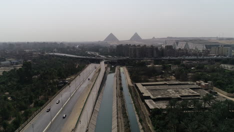 Aerial-Shot-for-The-Pyramids-of-Egypt-in-Giza-positioned-in-the-background-of-a-branch-from-the-River-Nile-in-the-foreground-Maryotya-branch