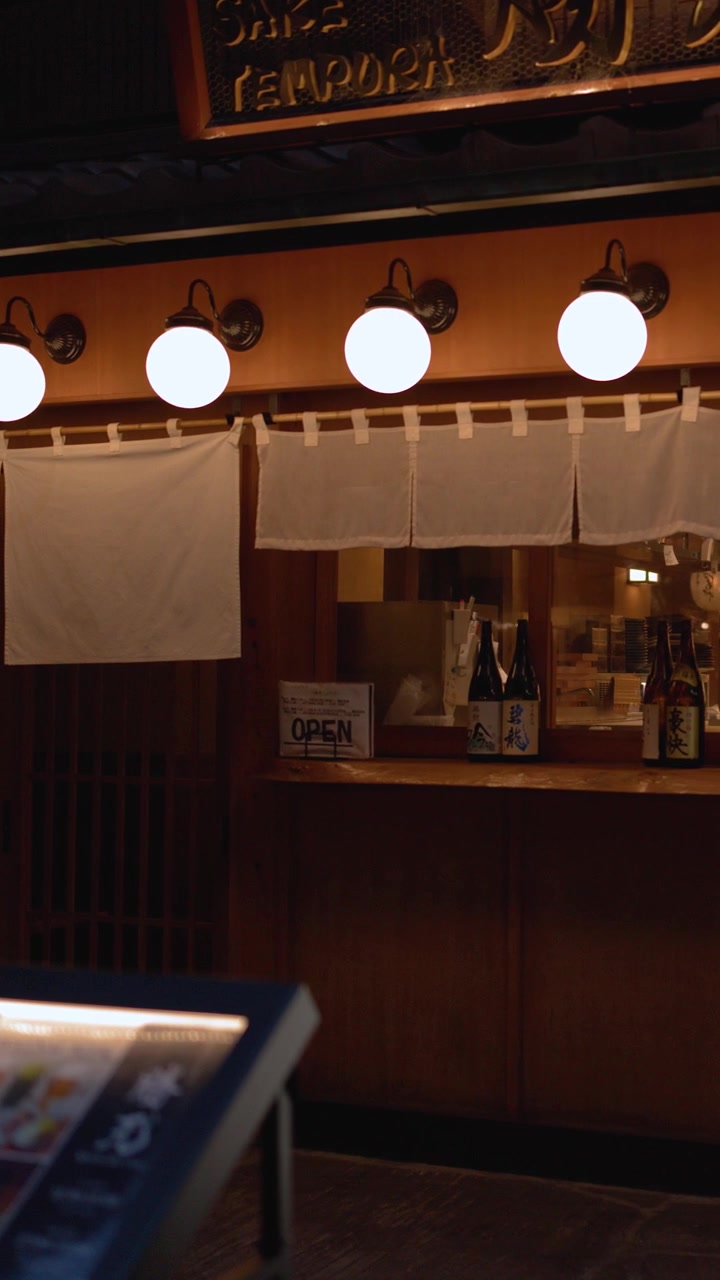 En langsom kamerapanorering afslører en traditionel japansk restaurantindgang med lanterner og sakeflasker.