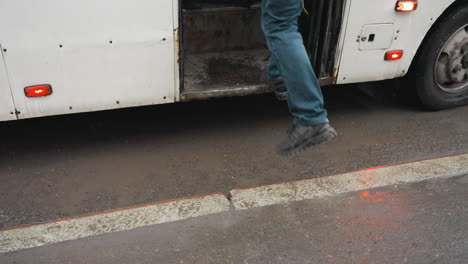 close-up of two individuals entering a parked white bus on a wet road. one person carries a black bag, and the bus door closes after entry