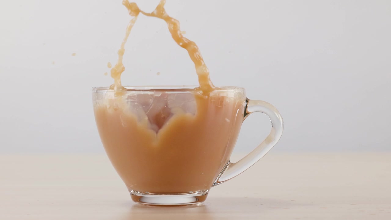 Schizzo al rallentatore mentre un cubetto di ghiaccio cade in una tazza di vetro di caffè latte su un tavolo