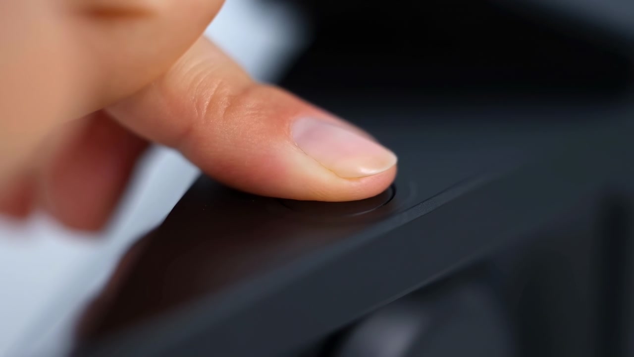 Caucasian Fingertip Pressing Power Button Gently, Closeup On Glossy Black Plastic Surface With Blue LED