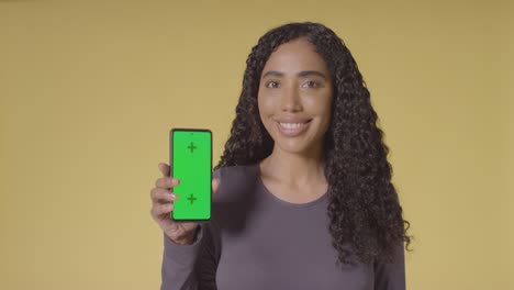 studio portrait of smiling woman holding up mobile phone with green screen