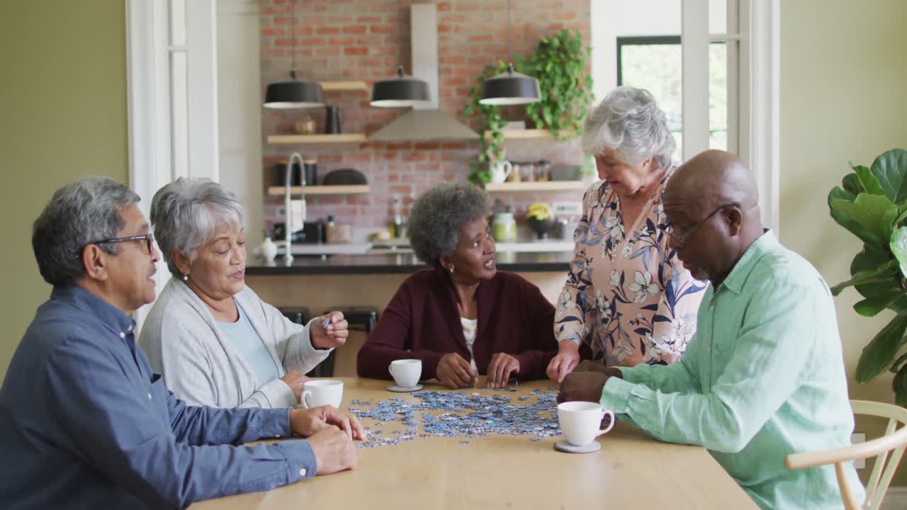 Group of happy diverse senior friends drinking coffee and doing puzzle at home