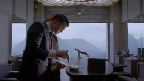 a man in a suit soldering a circuit board at a desk with a mountain view