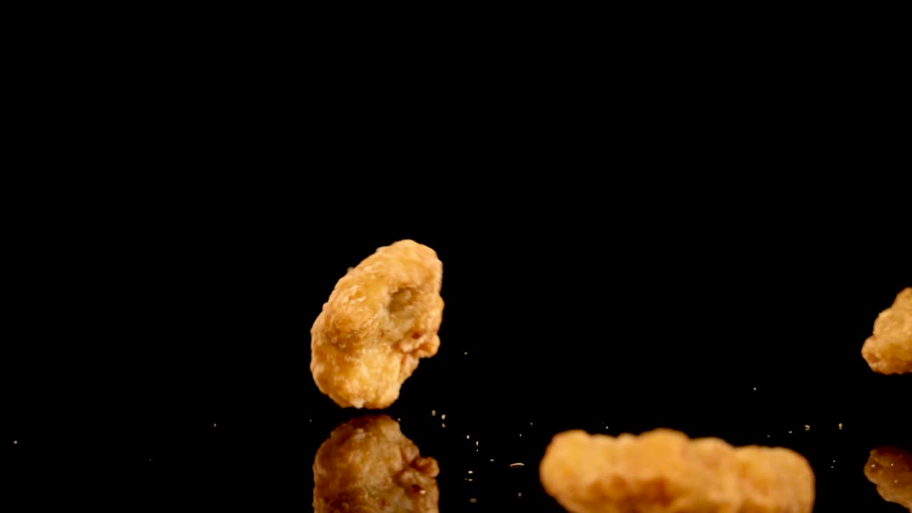 Golden fried chicken nuggets tumble and bounce onto a glossy black surface, captured in slow motion with dramatic lighting and high-speed camera movement