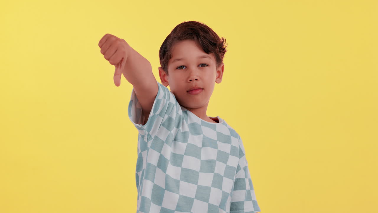 Boy giving thumbs down on yellow background