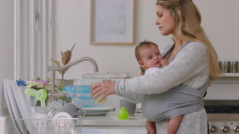 Schöne-Mutter-Mit-Baby,-Die-Zu-Hause-Arbeitet,-Geschirr-Wäscht,-Küche-Putzt,-Sich-Um-Das-Kleinkind-Kümmert,-Das-Hausarbeit-Erledigt-Und-Mutterschaft-Genießt