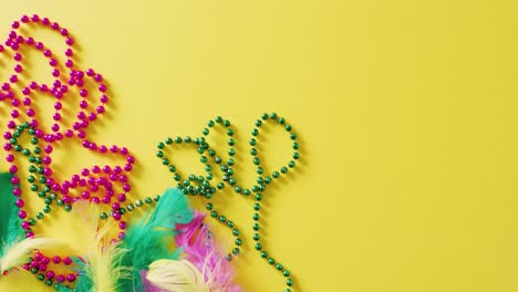 Video-of-pink-and-green-mardi-gras-carnival-beads-and-feathers-on-yellow-background-with-copy-space