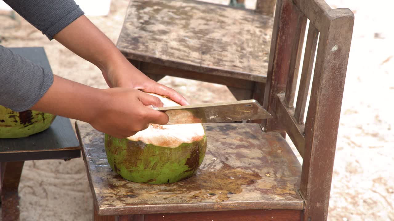 Primo piano di mani che spaccano abilmente una noce di cocco verde con una mannaia su una sedia