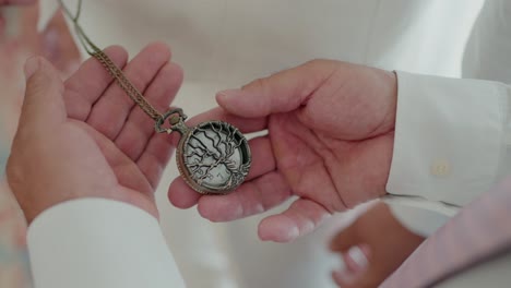 close-up of hands holding an antique pocket watch with a tree design on its cover, exchanging it as a sentimental gesture