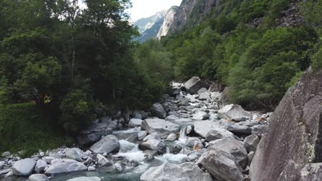 Aerial-backwards-host-of-rocky-river-with-maria-statue-in-Foroglio,-Switzerland