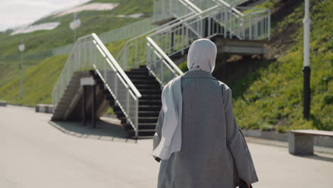 arabian woman adjusts hijab walking to stairs on hill slope