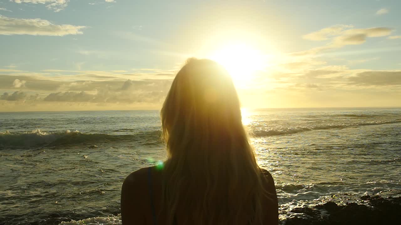 Kvinde set bagfra der ser solnedgangen og havet i Fransk Polynesien