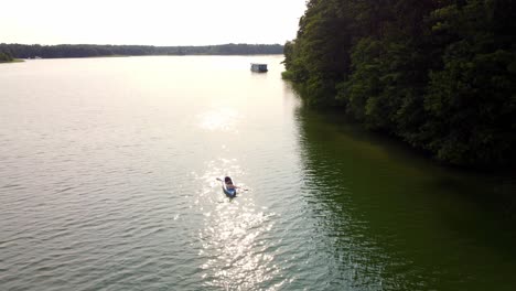 Person-riding-a-canoe-on-a-lake-next-to-a-forest-in-Brandenburg,-Germany