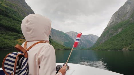 Eine-Person-Mit-Einer-Norwegischen-Flagge-In-Der-Hand-Reist-Auf-Einem-Schiff-Auf-Einem-Malerischen-Fjord