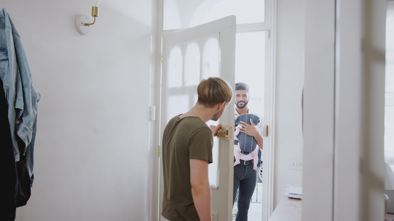 Same Sex Male Couple With Baby Daughter In Sling Opening Front Door Of Home