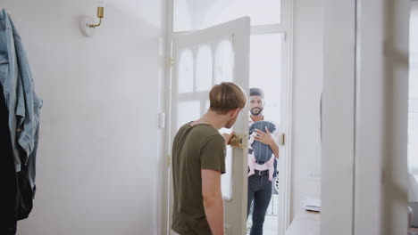 same sex male couple with baby daughter in sling opening front door of home