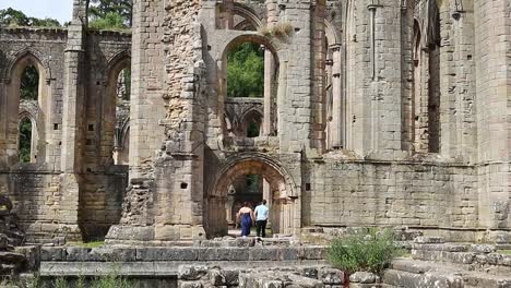 Couple-walking-Inside-walls-of-the-ruined-Cistercian-monastery,-Fountains-Abby-in-North-Yorkshire-UK