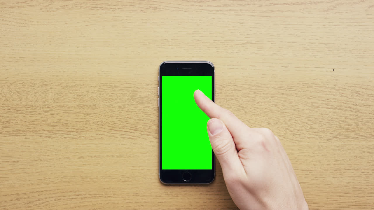Vista dall'alto: mani che usano un telefono cellulare touchscreen con gesti multi-touch su schermo verde, su una scrivania in legno - Red Epic Dragon