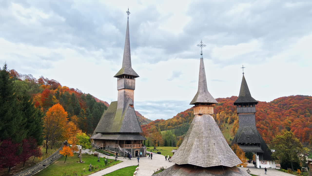 Aerial drone view of the Barsana Monastery, Romania. Main church and other buildings, visitors, hills covered with yellowing forest around