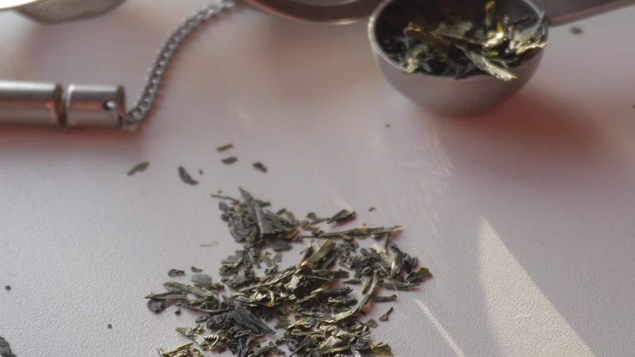 Fresh green tea leaves spread out with a tea infuser, captured in soft light