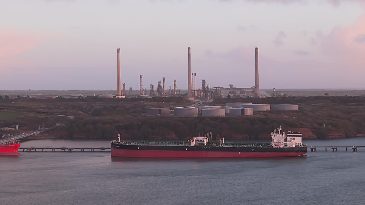 A large oil tanker approaches the Valero Pembroke Refinery, with industrial tanks and smokestacks visible in the background
