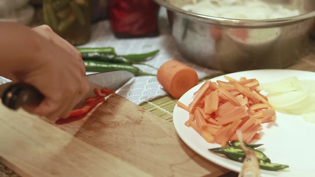 Person slicing red paprika into strips on a wooden chopping board for meal preparation in a kitchen
