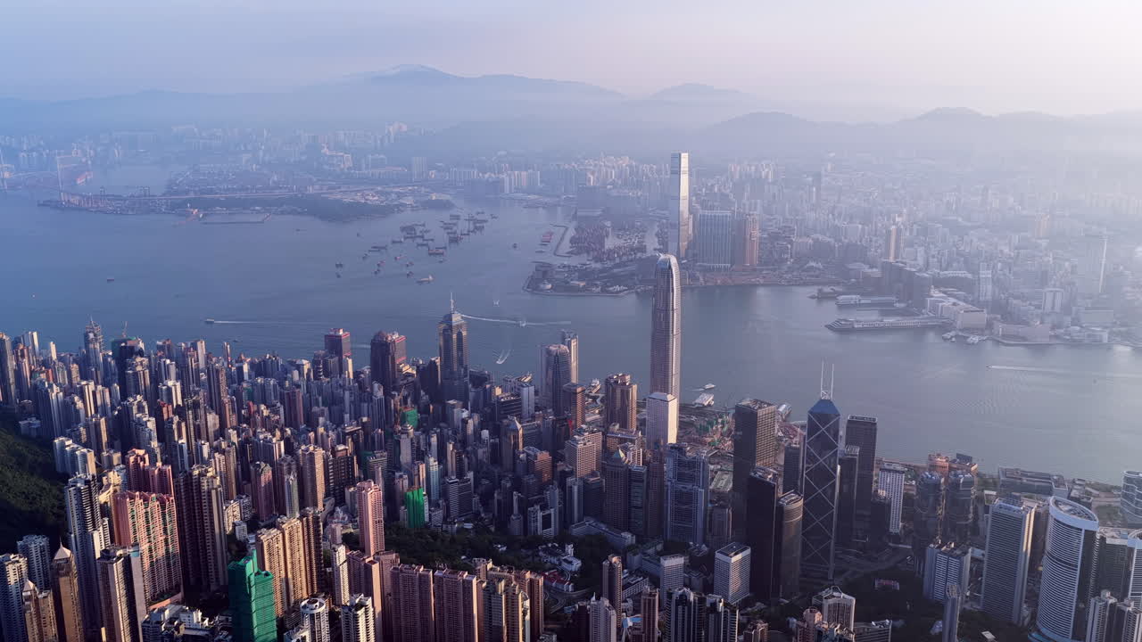 Cinematic aerial view of Hong Kong skyline shrouded in mist at blue hour, with glowing skyscrapers and Victoria Harbour fading into a moody, atmospheric twilight