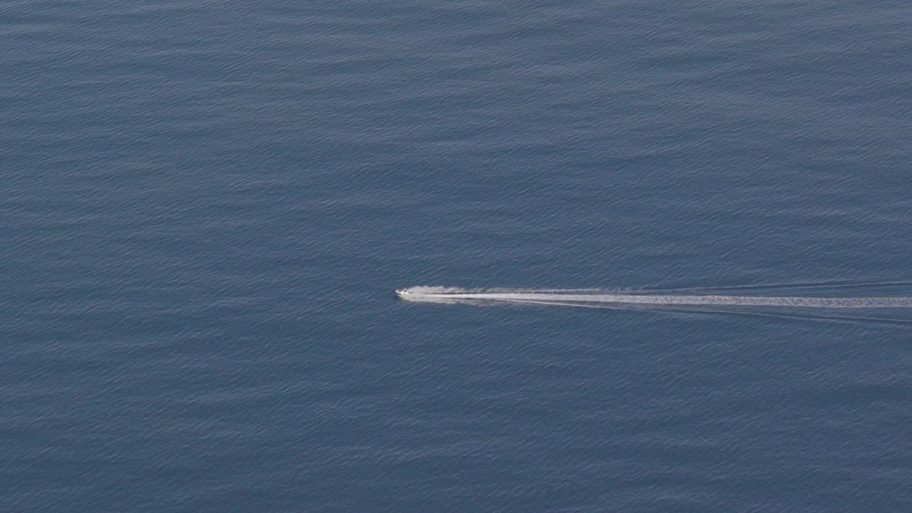 Ripresa statica con drone di una moto d'acqua che sfreccia sull'oceano lasciando una scia bianca vicino allo skyline di Itapema, Santa Catarina, Brasile in lontananza