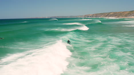 Aerial:-Surfing-the-beach-of-Bordeira-in-the-Algarve,-Portugal