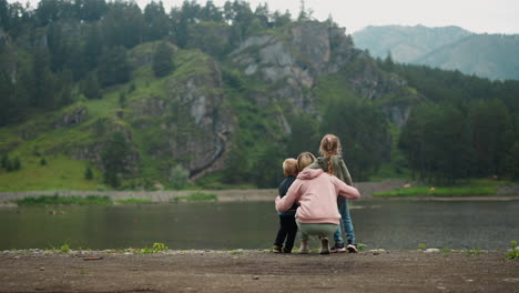 mother hugs little children on calm river bank at highland