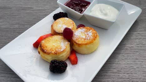 Köstliche-Syrniki-Mit-Waldbeeren-Und-Sauerrahm,-Mini-Hüttenkäse-Pfannkuchen-Zum-Frühstück,-Traditionelles-Ukrainisches-Russisches-Gericht,-Brunch-Restaurant,-4K-Aufnahme