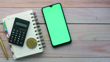 calculator, notebook, smartphone, and bitcoin on wooden table