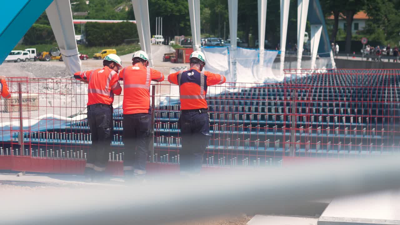 Workers in safety gear inspect bridge rigging at a construction site in sunny southern France