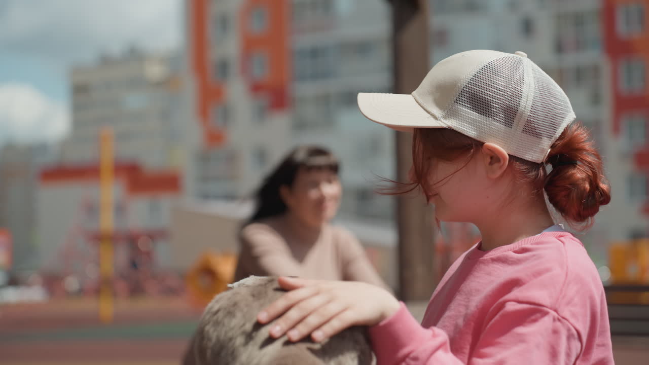 Child Holds Cat On Park Bench, Youthful White Girl Provides Tender Hug To Beloved Feline Companion, Young Girl Wearing Pink Clothing Shares Trusting Moment While Cuddling Her Cat On Urban Bench