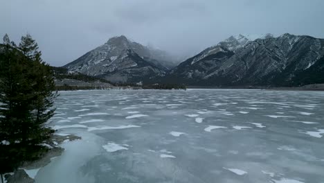 aerial ascent of frozen lake with mountains, alberta, canada