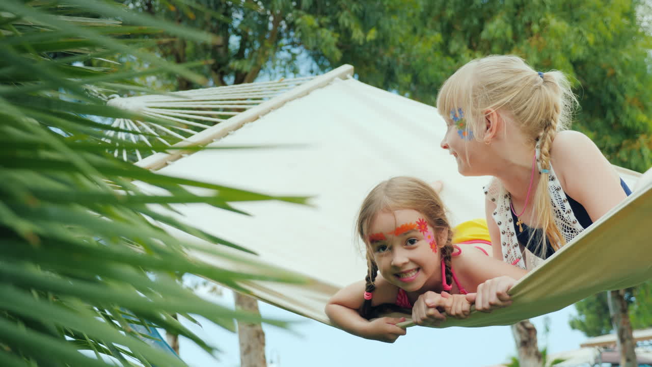 две классные девушки с аквагримом на лице развлекаются игрой в гамаке на территории туристического хот