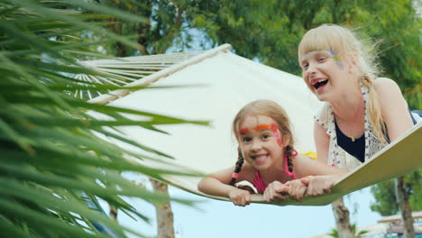 Two-Cool-Girls-With-Aquagrim-On-The-Face-Have-Fun-Play-A-Hammock-On-The-Territory-Of-The-Tourist-Hot