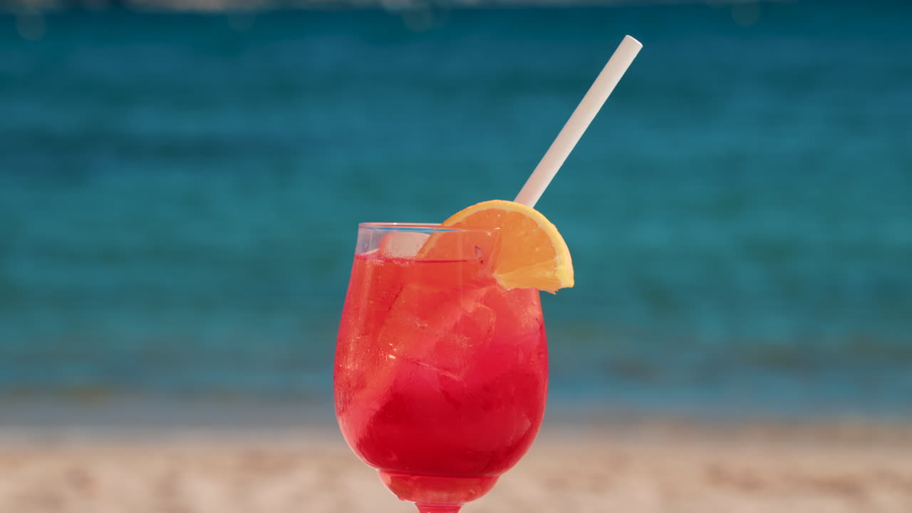 Refreshing red orange cocktail with ice and orange slice against the deep blue Mediterranean Sea