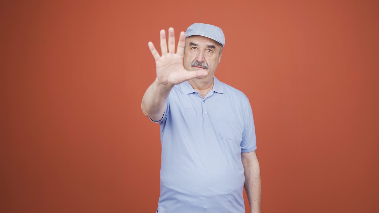 un anciano haciendo una señal de alto para la cámara.