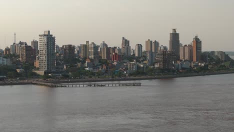 Toma-Aérea-Amplia-Que-Muestra-El-Tráfico-En-La-Carretera-Costera-De-La-Ciudad-De-Posadas-Con-Edificios-De-Gran-Altura-Al-Atardecer,-Argentina