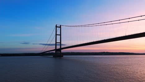 a picturesque spectacle unfolds as humber bridge stands adorned in the colors of the setting sun, with cars gracefully navigating its span