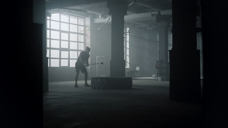 athlete beating rubber tire with hammer. man with sledgehammer doing workout